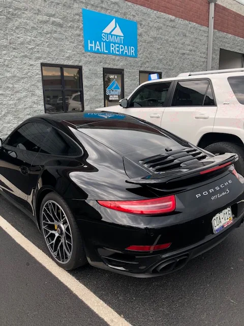 Black Porsche 911 Turbo S parked outside the Summit Hail Repair shop