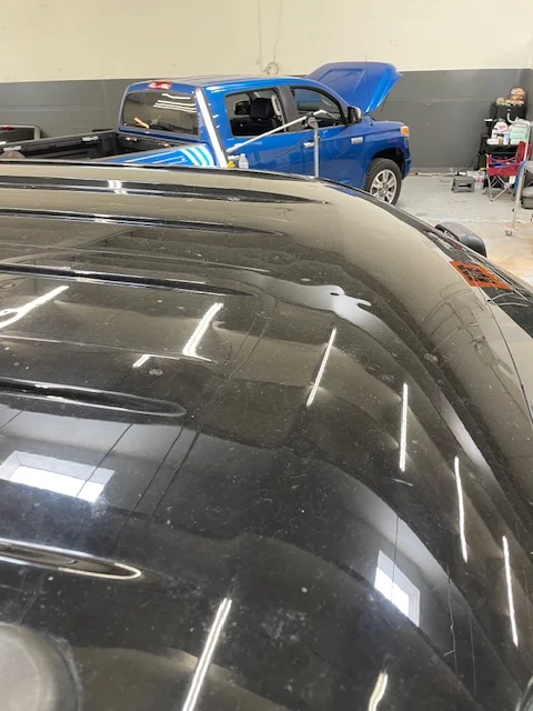 Black roof panel being inspected with a blue Tundra in the background