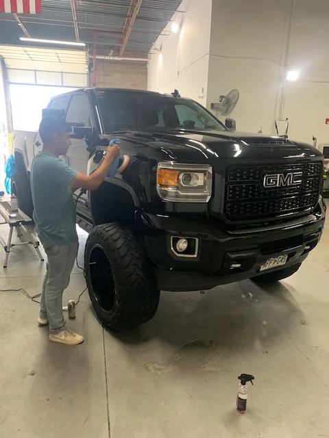 Technician polishing the fender of a black GMC Denali truck